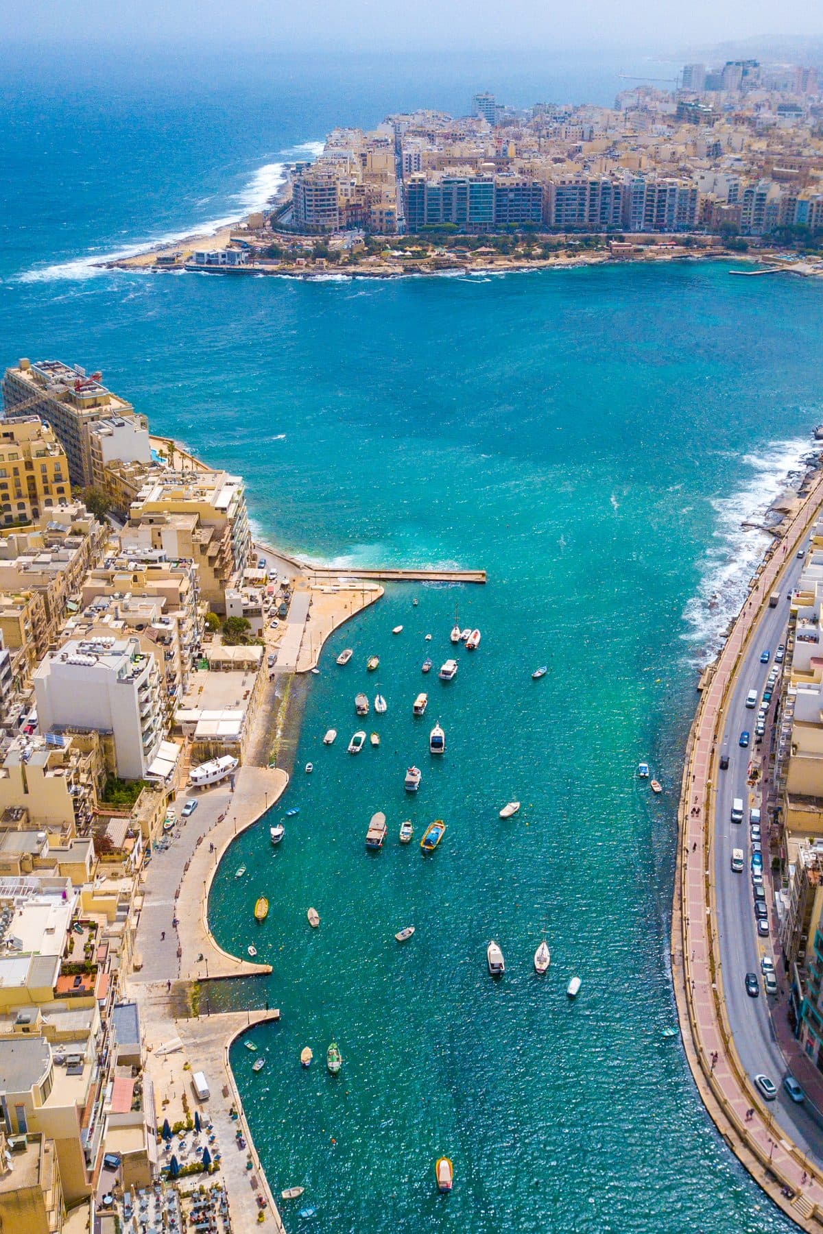 Spinola Bay from above, fishing boats moored along the curved quay at St Julian's with the coast running out behind it.